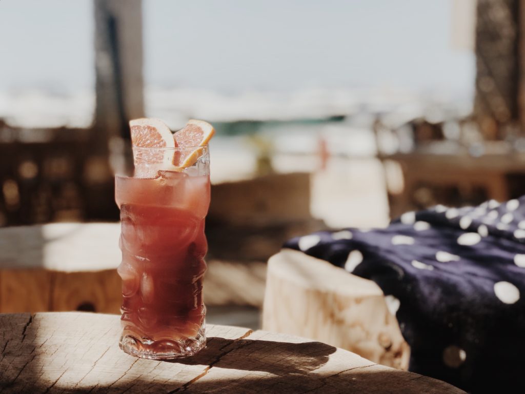 Fresh fruit red cocktail with mint, pomegranate, lemon in glass on beach background