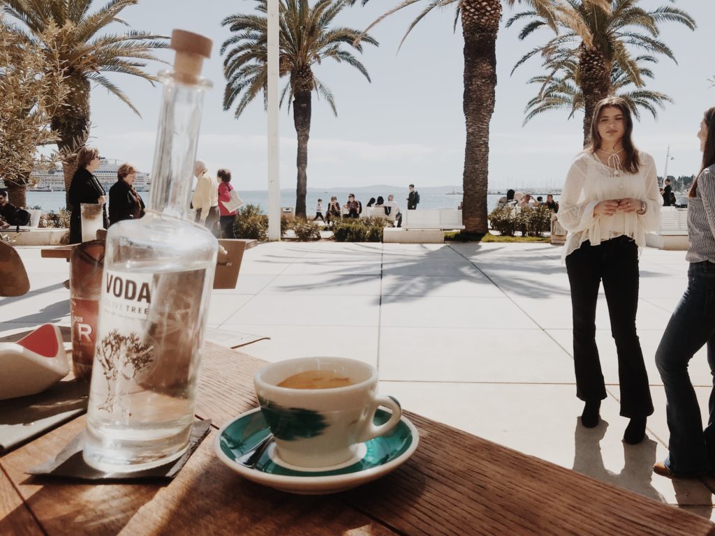 A bottle of water and a cup of coffee with palms in the backgroundn background